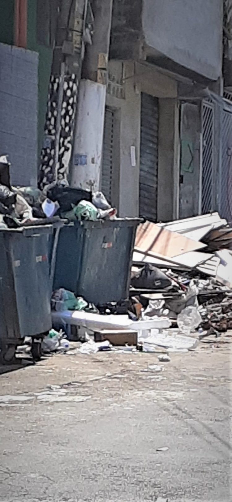 Caçamba está lotada e ao redor há muito entulho depositado